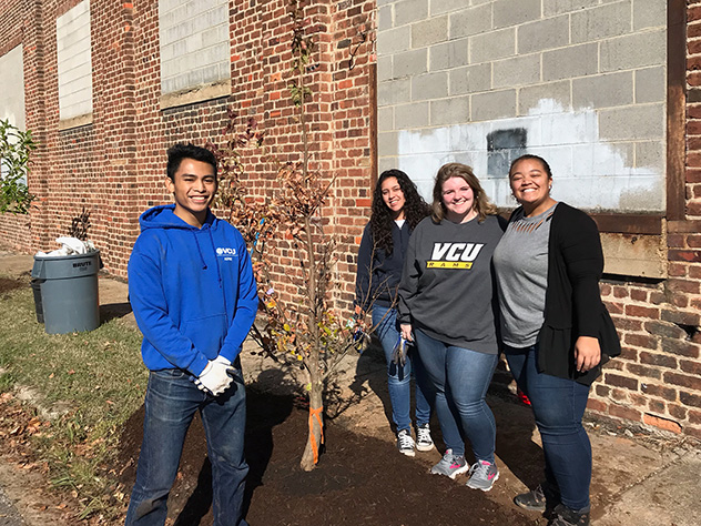 Courtney LaTourrette stands outside in with a group of three other people, next to a brick building and recently planted tree
