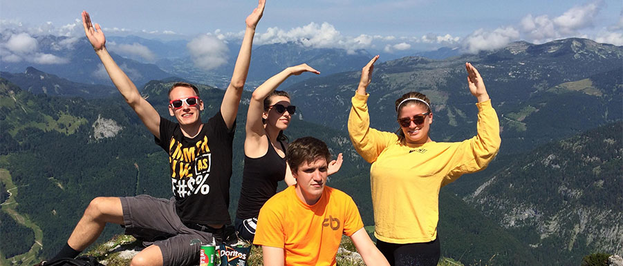 four v.c.u. students standing against a backdrop of austrian mountains making out the v.c.u. letters with their arms