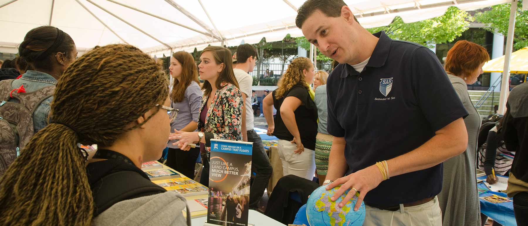 An instructor at a fair holding a globe and talking to an eager young listener.