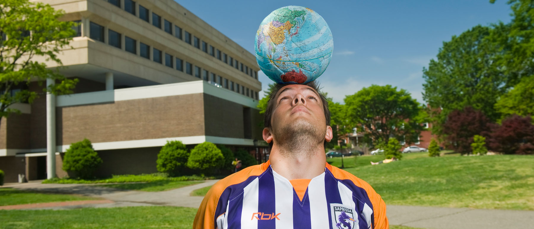 soccer player balancing a globe on top of his head in front of harris hall at v.c.u.