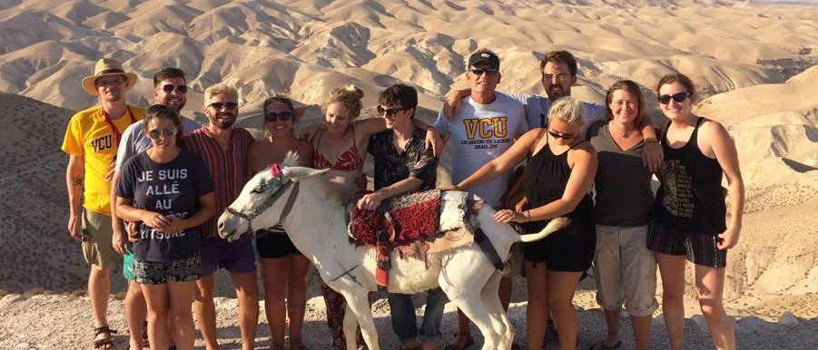 a group of happy v.c.u. students posing in a desert in israel accompanied by a small horse