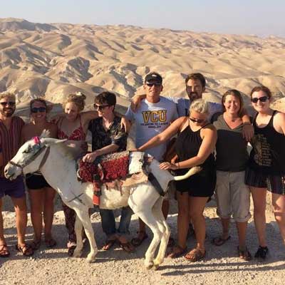 a group of happy v.c.u. students posing in a desert in israel accompanied by a small horse