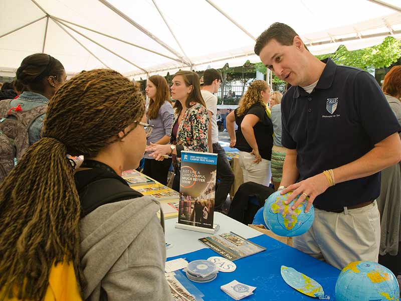 An instructor at a fair holding a globe and talking to an eager young listener.