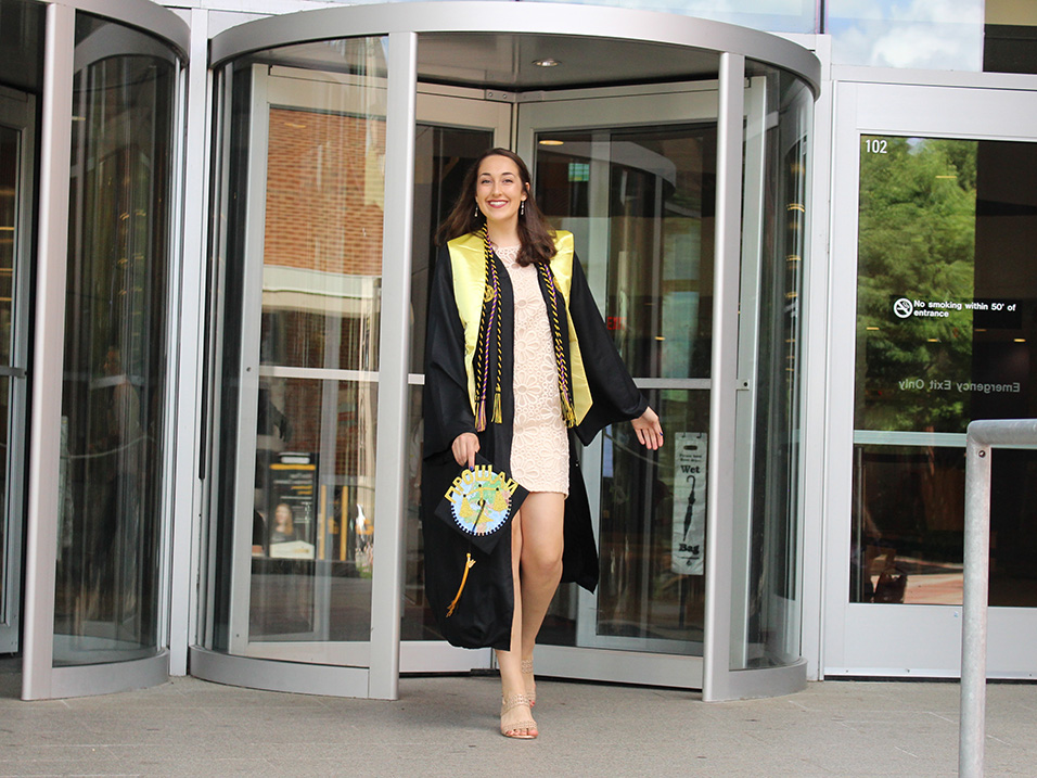 Marina Pugh steps out of a revolving door wearing graduation regalia